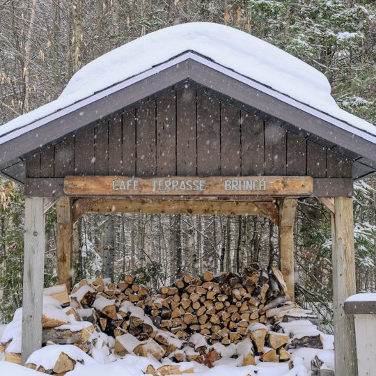 Abri à bois du Domaine sous la neige, surmonté de son enseigne Café Terrasse Brunch